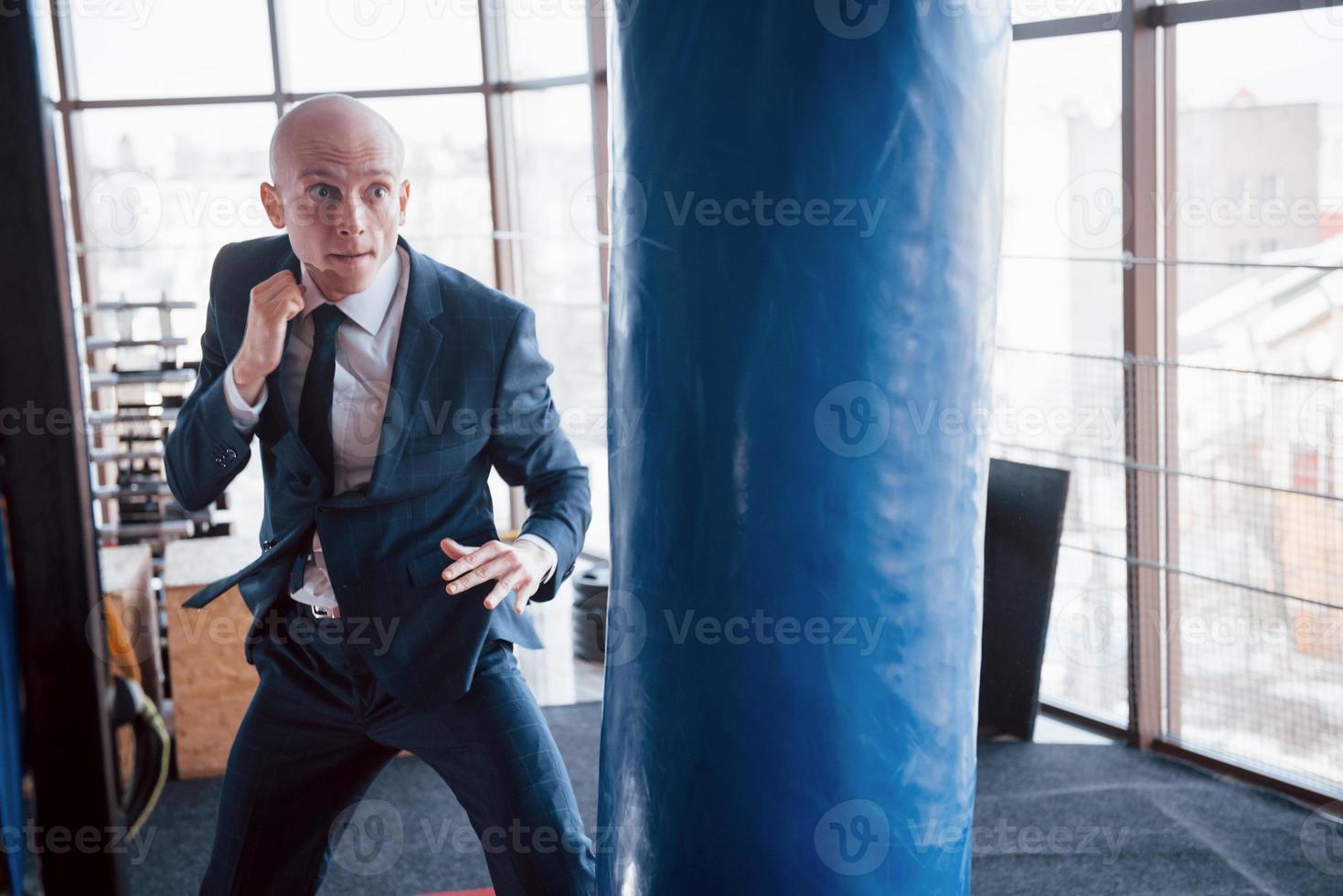 un homme d'affaires chauve en colère bat une poire de boxe dans la salle de sport. concept de gestion de la colère photo