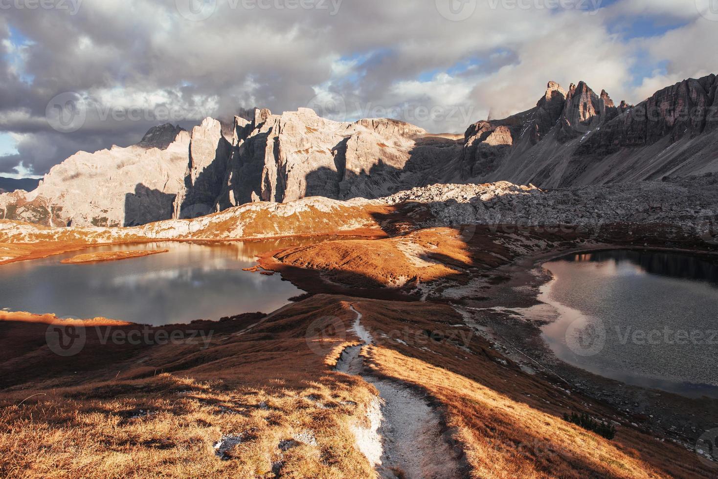 le chemin entre deux petits lacs allant aux grandes montagnes de dolomie debout au soleil photo