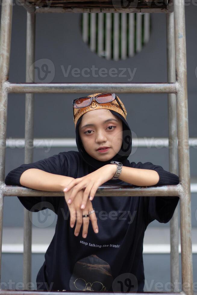 un asiatique femelle modèle des stands en toute confiance sur une tennis rechercher, habillé dans jeans et une noir chemise, orné avec une bandana et des lunettes photo