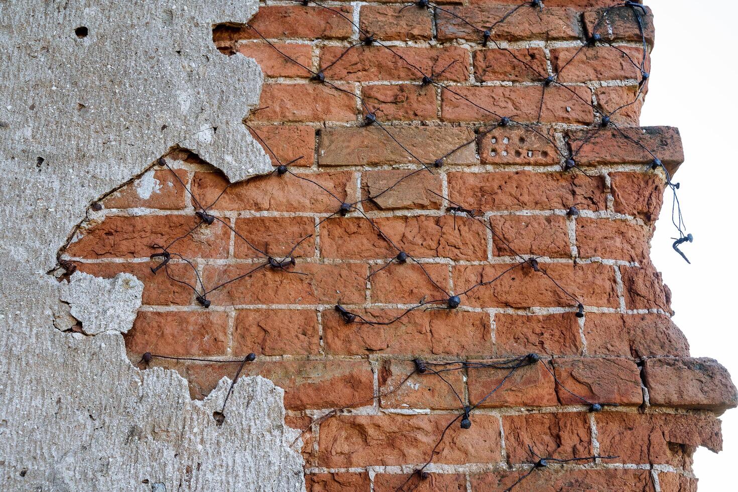 ancien maçonnerie, le vieux mur est fabriqué de rouge brique, forgé ongles sont conduit dans le mur, câble est blessure sur ongles fragment de plâtre de le mur, historique bâtiment photo