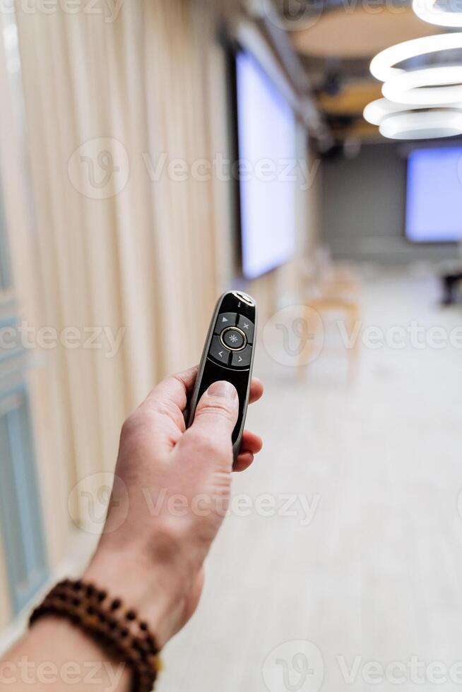 une main détient une sans fil clicker à présent diapositives sur le projecteur écran dans une conférence chambre. affaires événement, gadget dans une homme main. presse le bouton avec votre doigt. photo