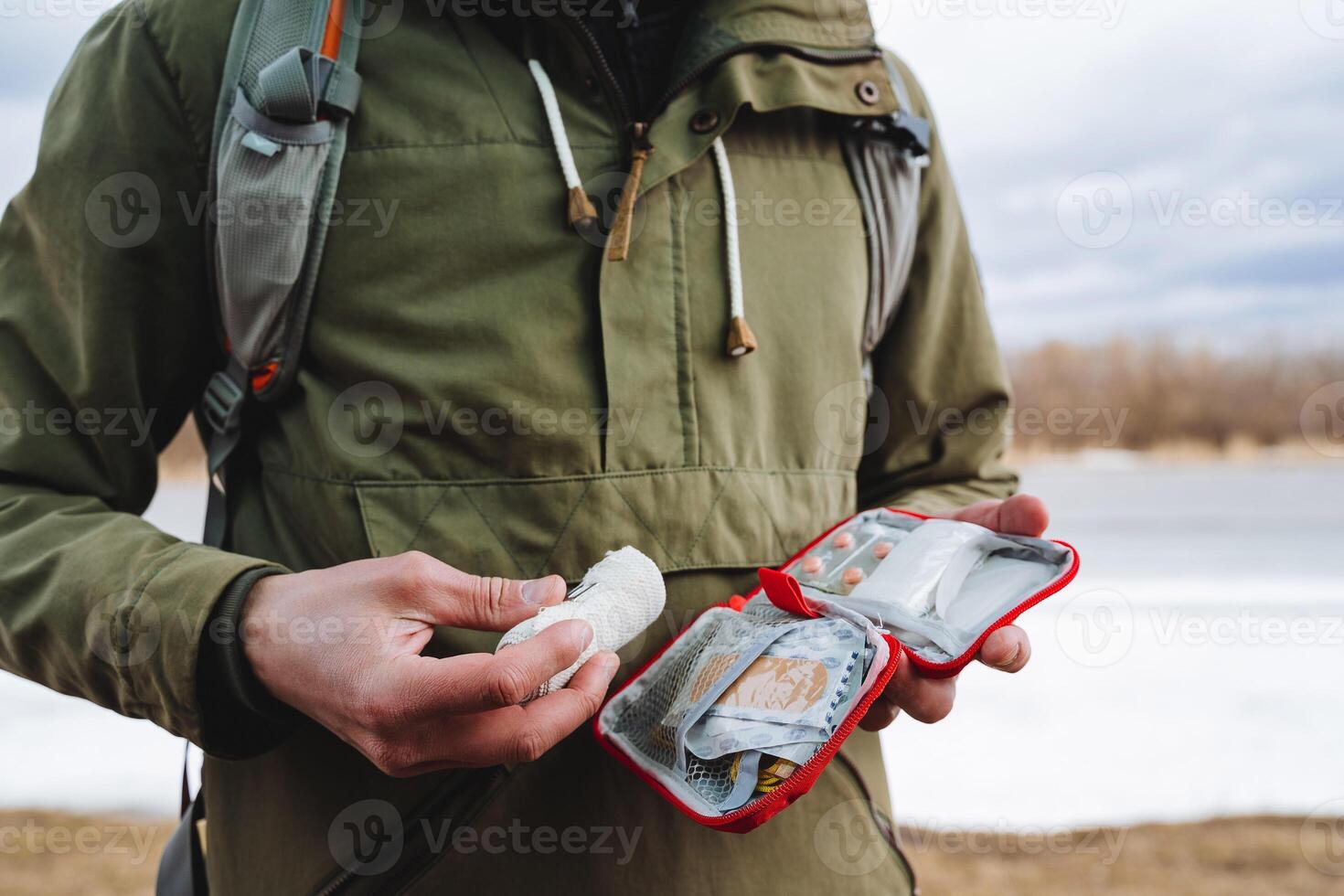 premier aide trousse, une ensemble de divers médicaments collecté dans une rouge sac, pilules pour douleur, un élastique bandage, une homme détient une premiers secours trousse dans le sien mains, randonnée équipement. photo