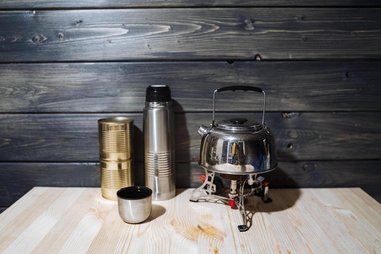 une ensemble de camping ustensiles. portable brûleur, bouilloire, thermos et en conserve aliments. camping, en mangeant en plein air. gaz brûleur photo