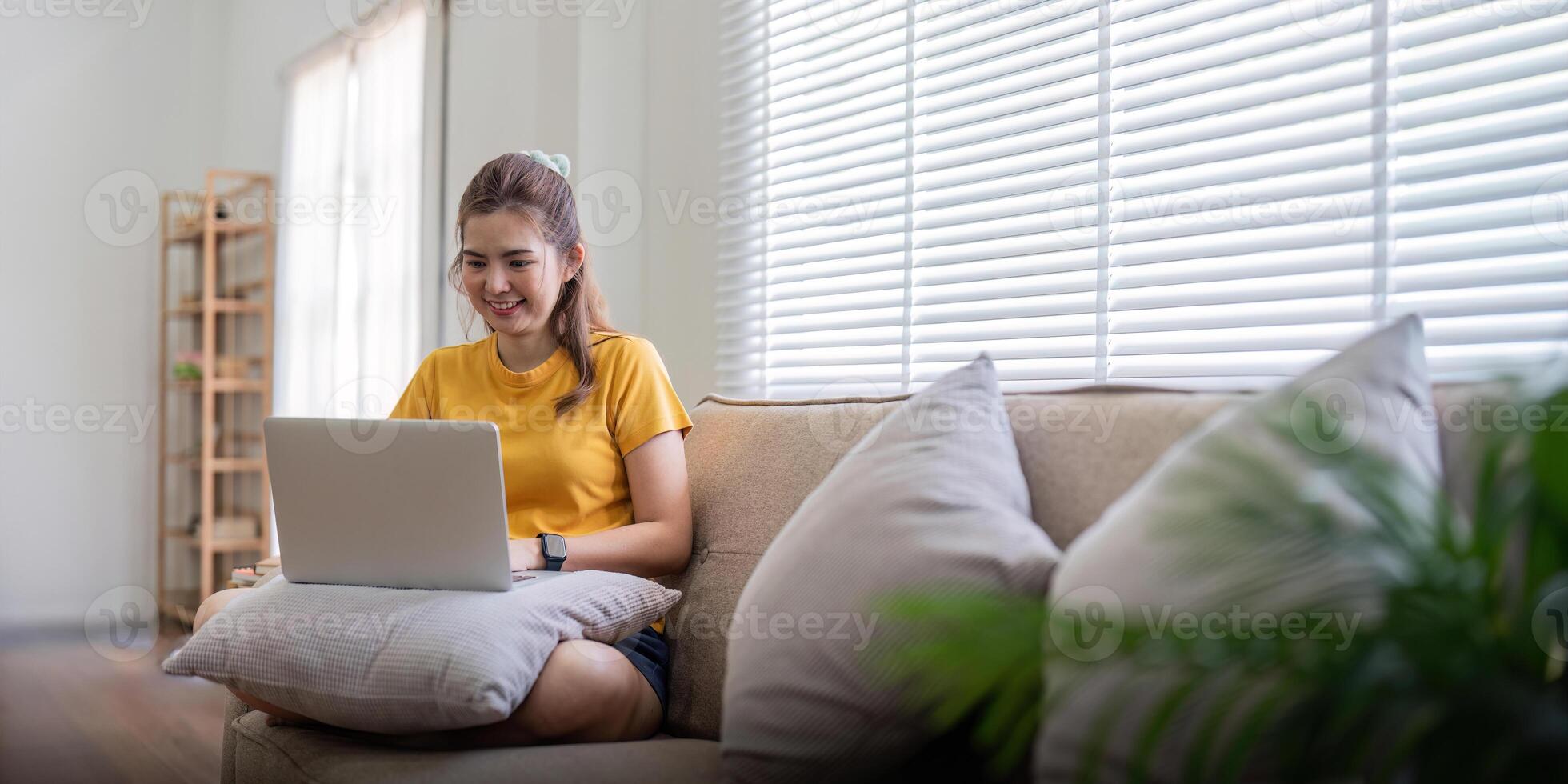 Jeune femme séance sur le canapé et travail sur projet, en train de regarder film sur portable du repos et content bavardage avec ami dans social réseau à Accueil photo