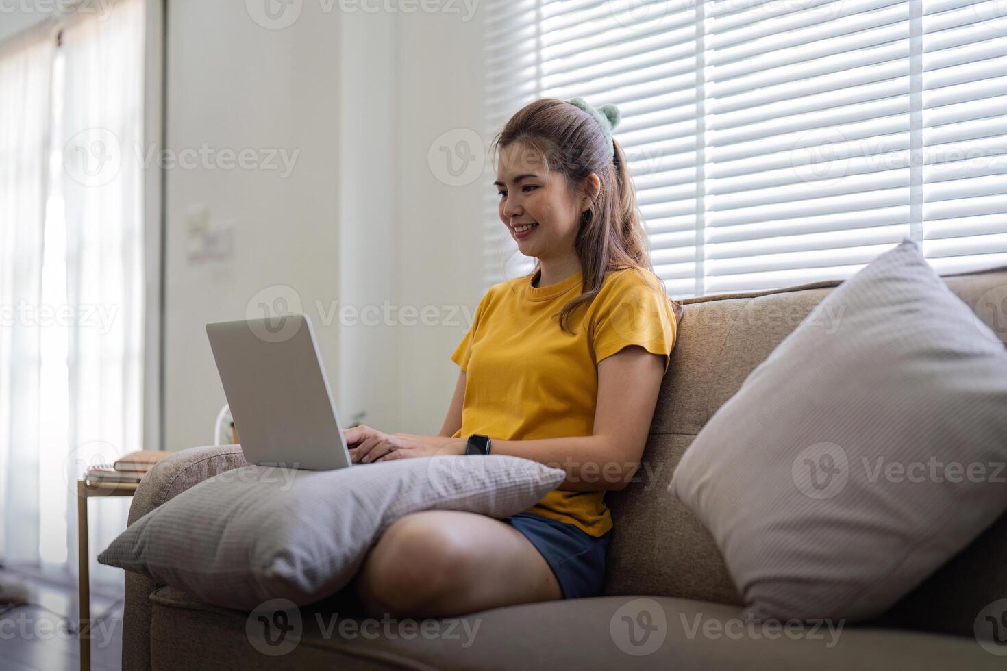 Jeune femme séance sur le canapé et travail sur projet, en train de regarder film sur portable du repos et content bavardage avec ami dans social réseau à Accueil photo