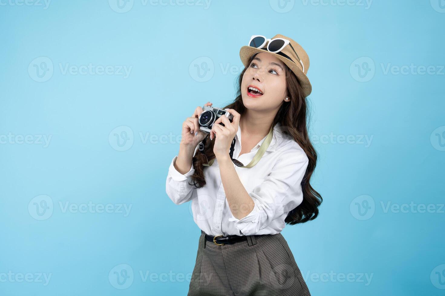 magnifique asiatique touristique dans décontractée vêtements est en portant une caméra avec une valise pour une Nouveau voyage dans une photo studio sur une bleu Contexte.