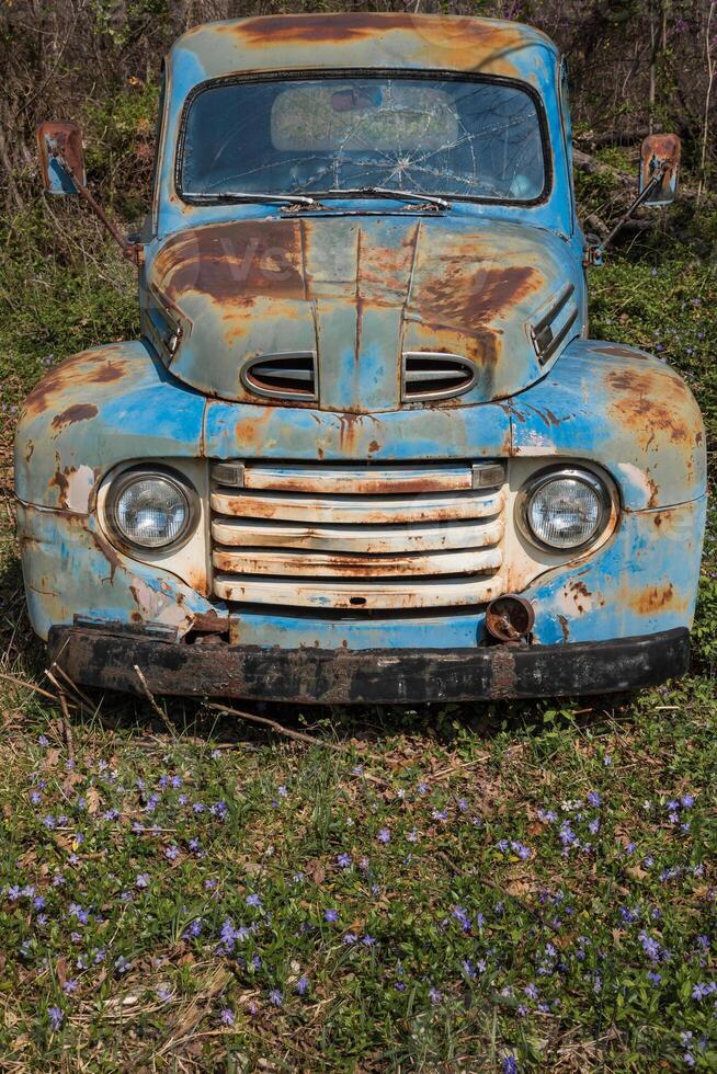 abandonné vieux bleu voiture dans une champ avec fleurs sauvages et herbe photo