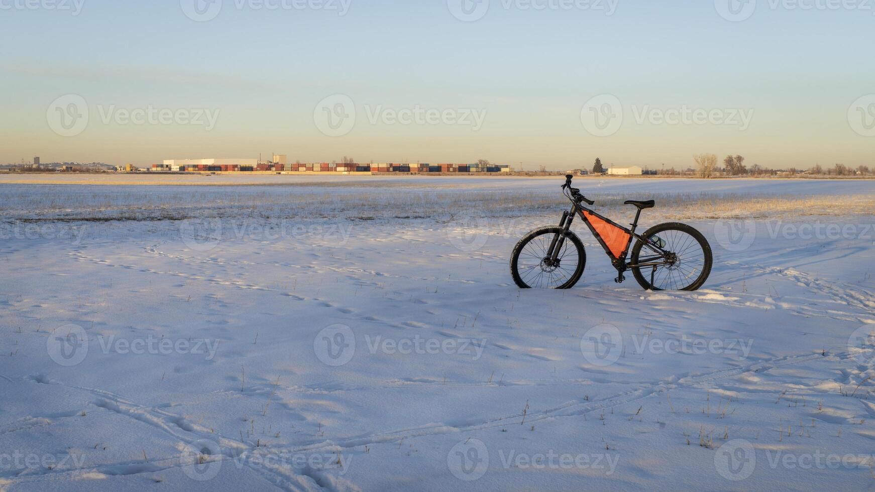 Montagne bicyclette à hiver le coucher du soleil sur une champ couvert par neige avec industriel zone dans Contexte photo