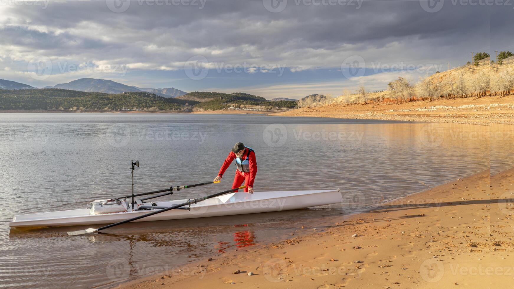 Sénior rameur est gréement le sien aviron coquille sur une rive de charretier Lac dans nord Colorado dans hiver paysage photo