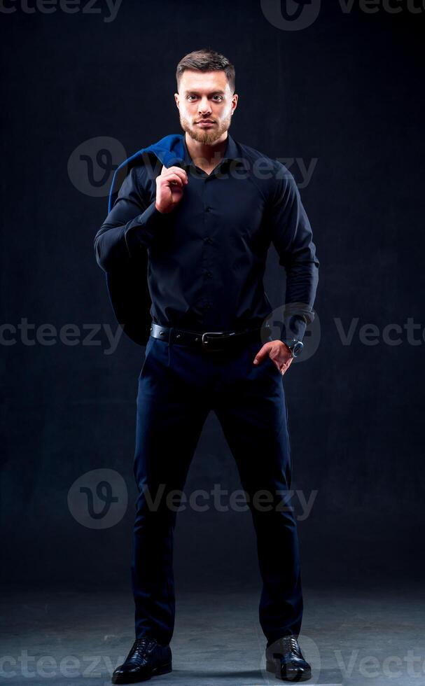 mode portrait de Jeune homme dans noir chemise. homme pose plus de foncé mur avec un main dans poche. Beau sur de soi homme, homme d'affaire, moderne vêtements. photo