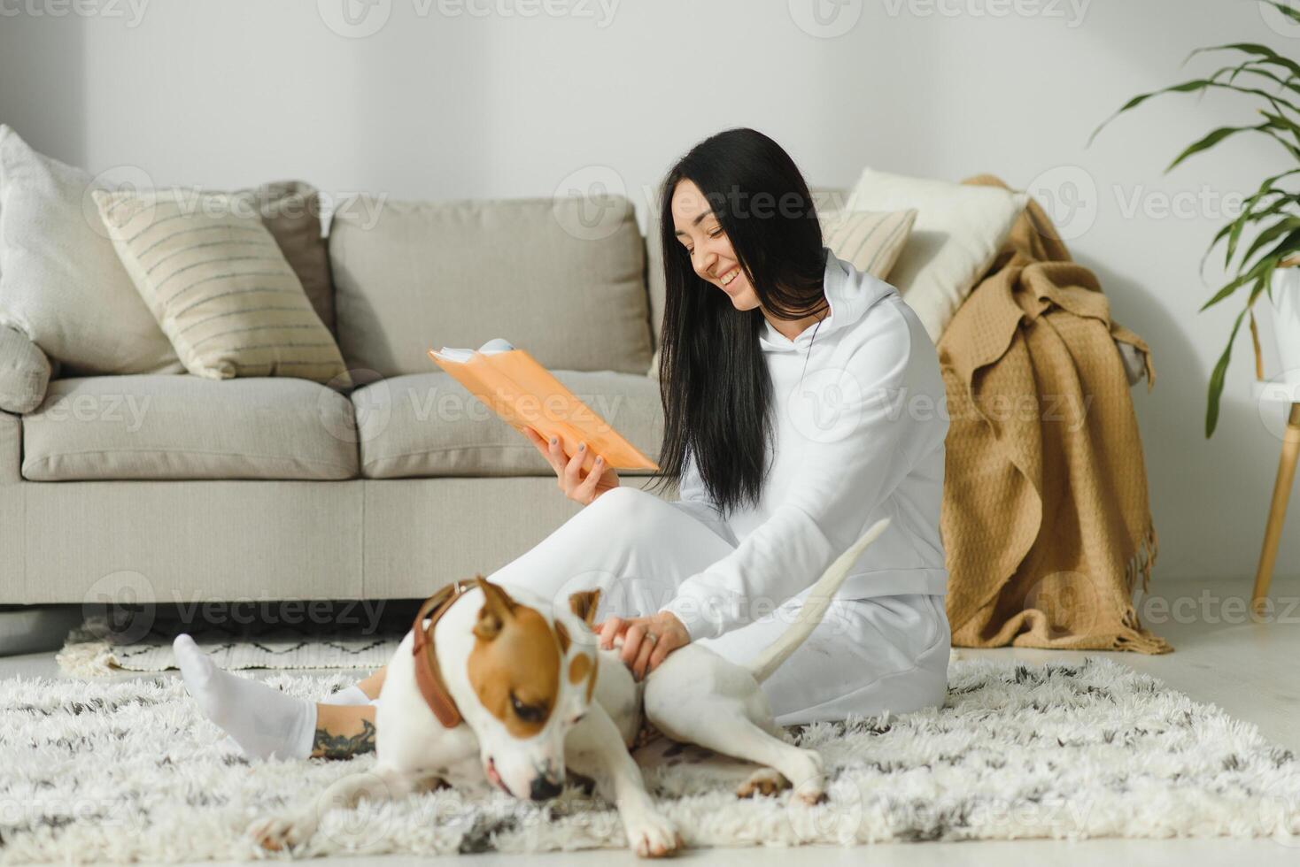 fille en train de lire une livre avec sa chien à côté de son. femme lit une livre avec chien sur le sol photo