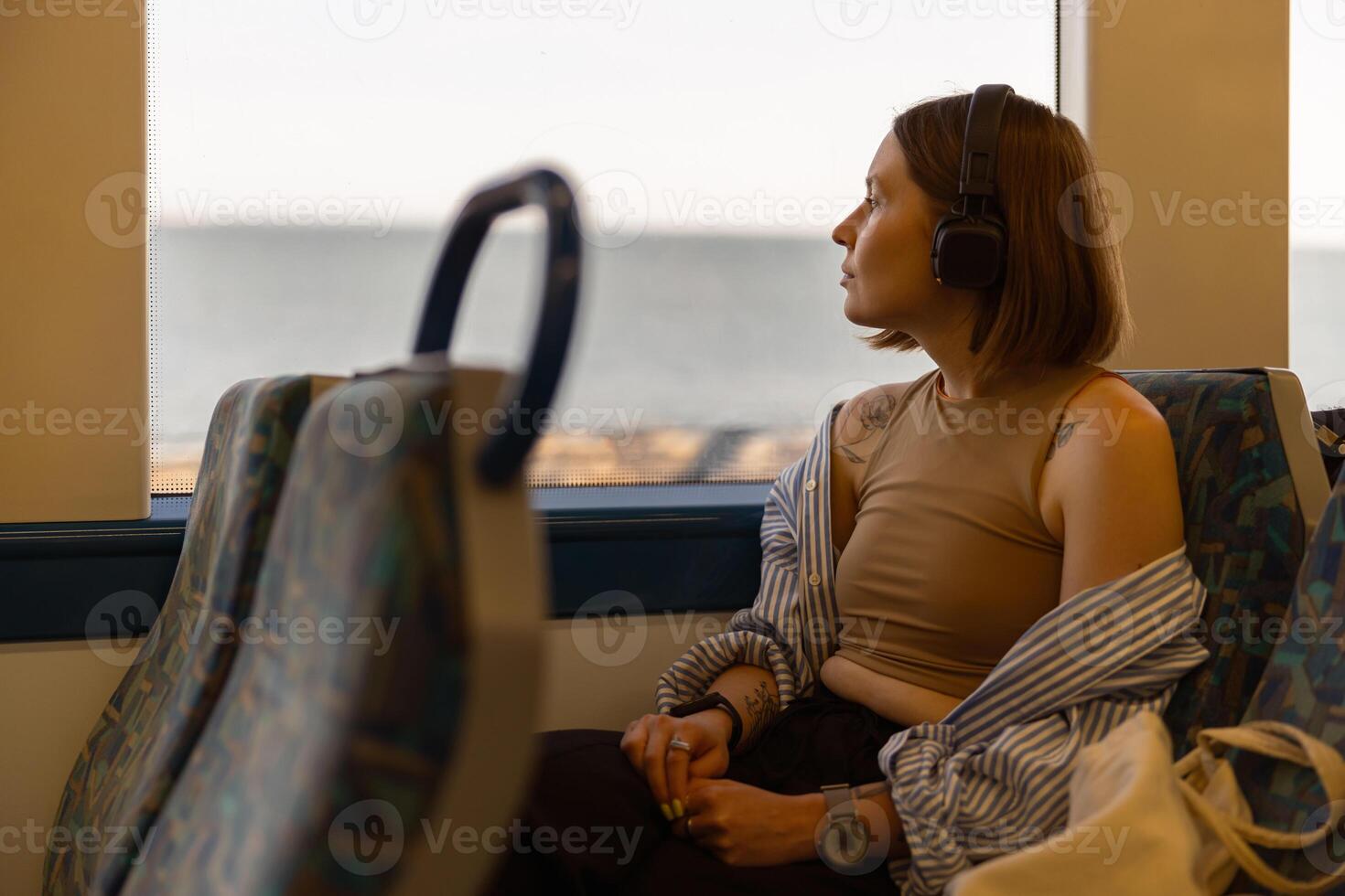femme dans écouteurs tandis que en voyageant dans Publique transport et à la recherche vue à l'extérieur le fenêtre photo