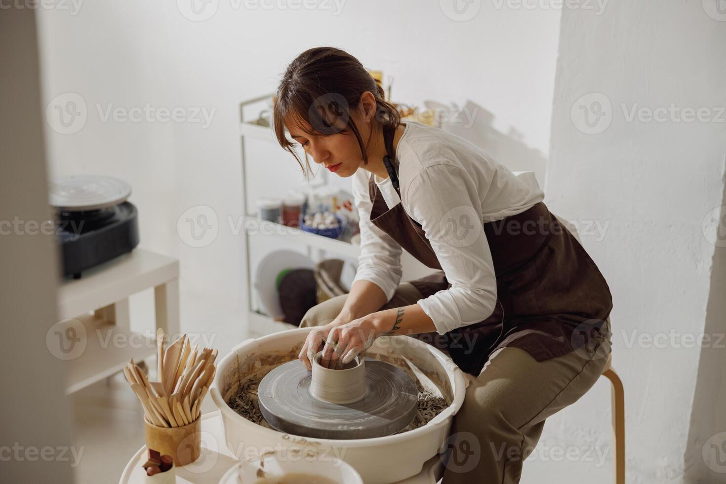 concentré femelle artisan dans tablier séance sur banc avec poterie roue et fabrication argile pot photo
