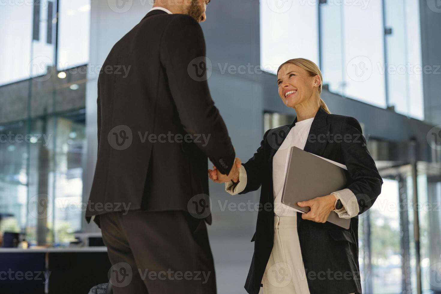 affaires les partenaires dans costume tremblement mains dans de face de le moderne bâtiment Contexte photo