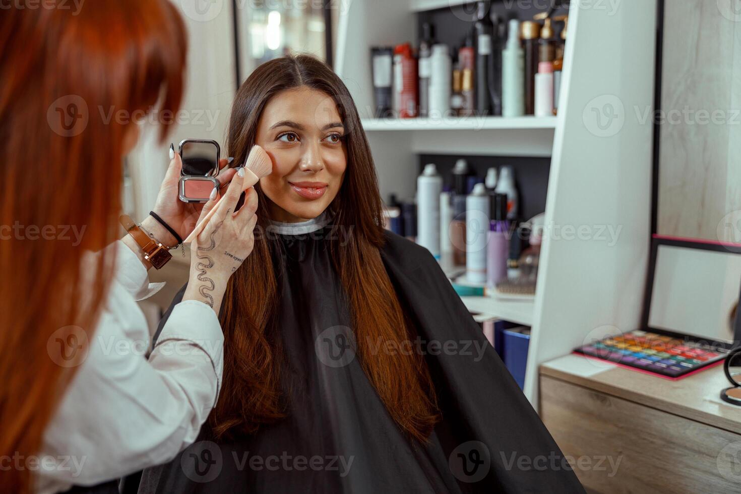 Jeune femelle client avoir maquillage rougir poudre sur sa joue avec une brosse photo