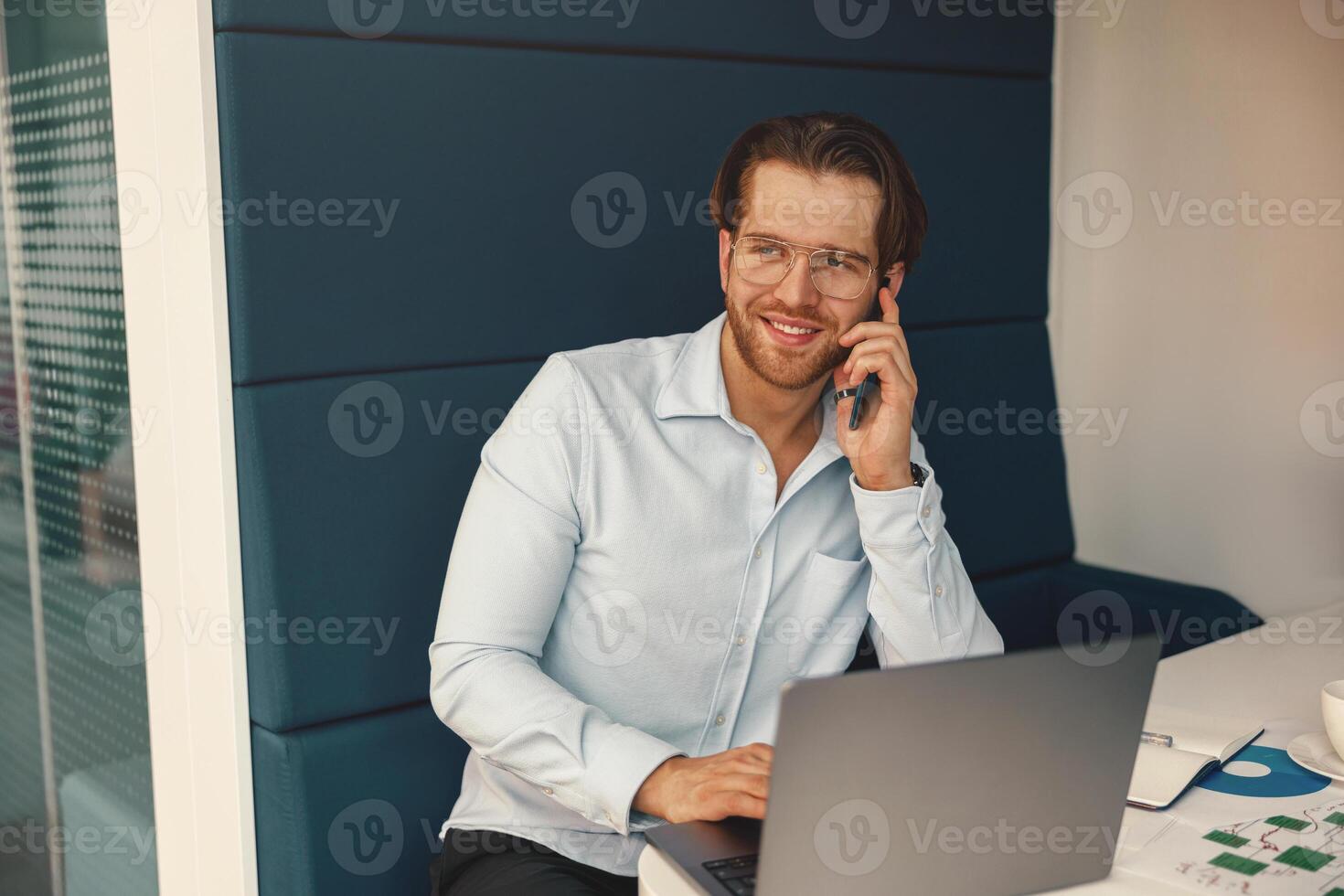 Masculin patron parlant téléphone avec client tandis que séance dans cotravail espace et travail sur portable photo