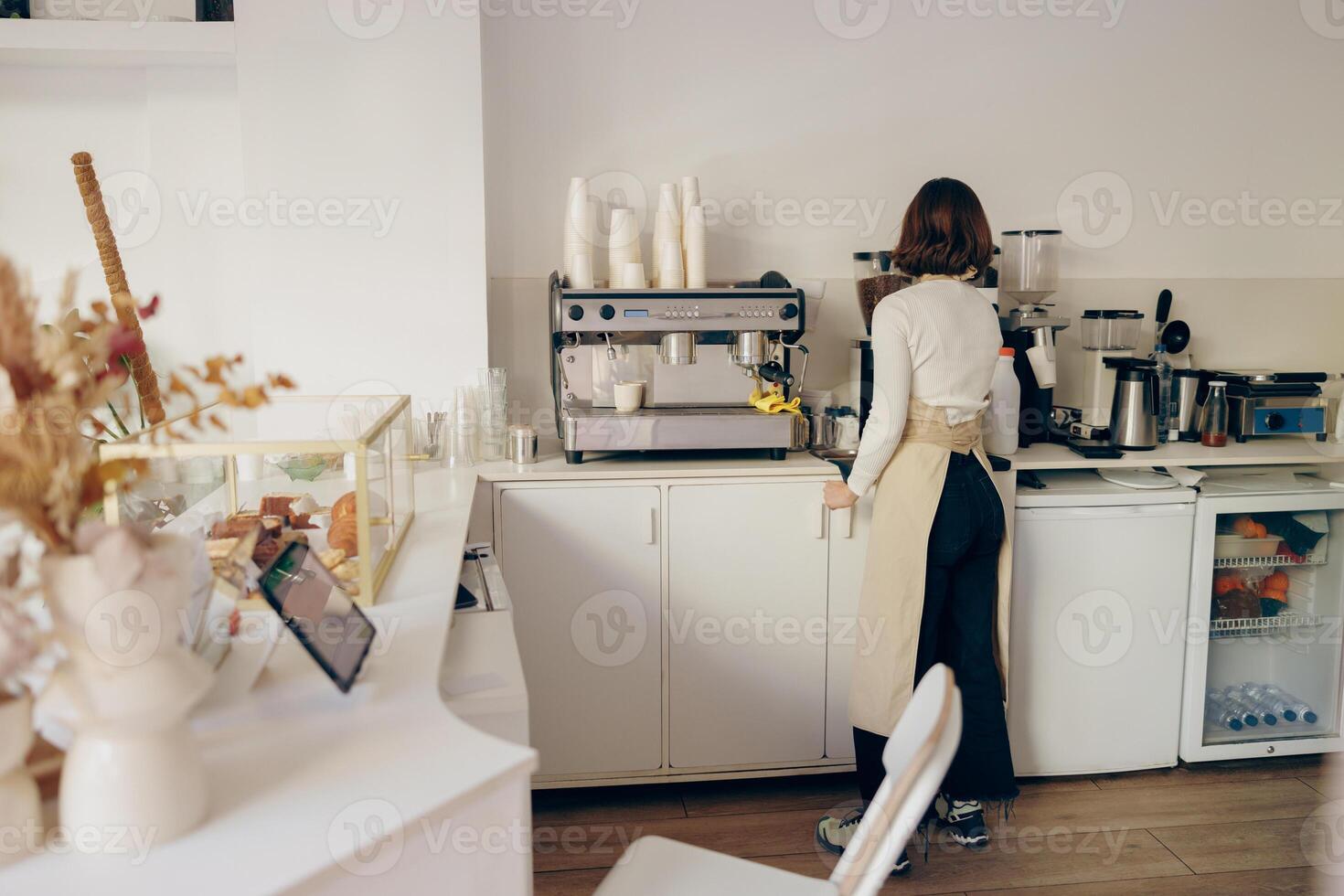 retour vue de femelle barista broyage café en utilisant professionnel broyeur machine dans café maison photo