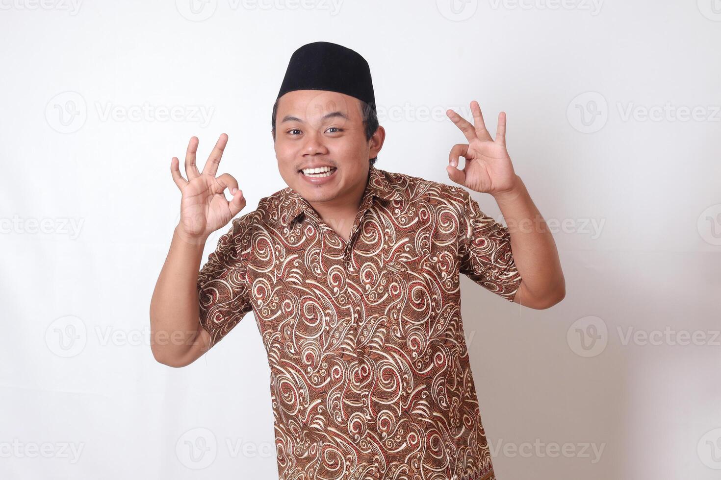 portrait de excité asiatique homme portant batik chemise et Songkok montrant D'accord main geste et souriant à la recherche à caméra. isolé image sur gris Contexte photo