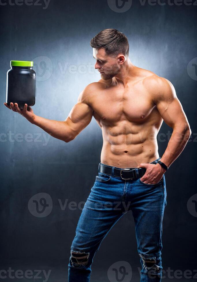 Masculin athlète bodybuilder avec une nu torse des stands avec une pot de des sports nutritionnel suppléments. photo