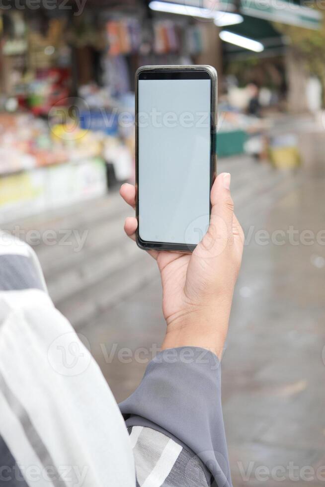 en portant intelligent téléphone avec vide écran avec flou café rue Contexte. photo