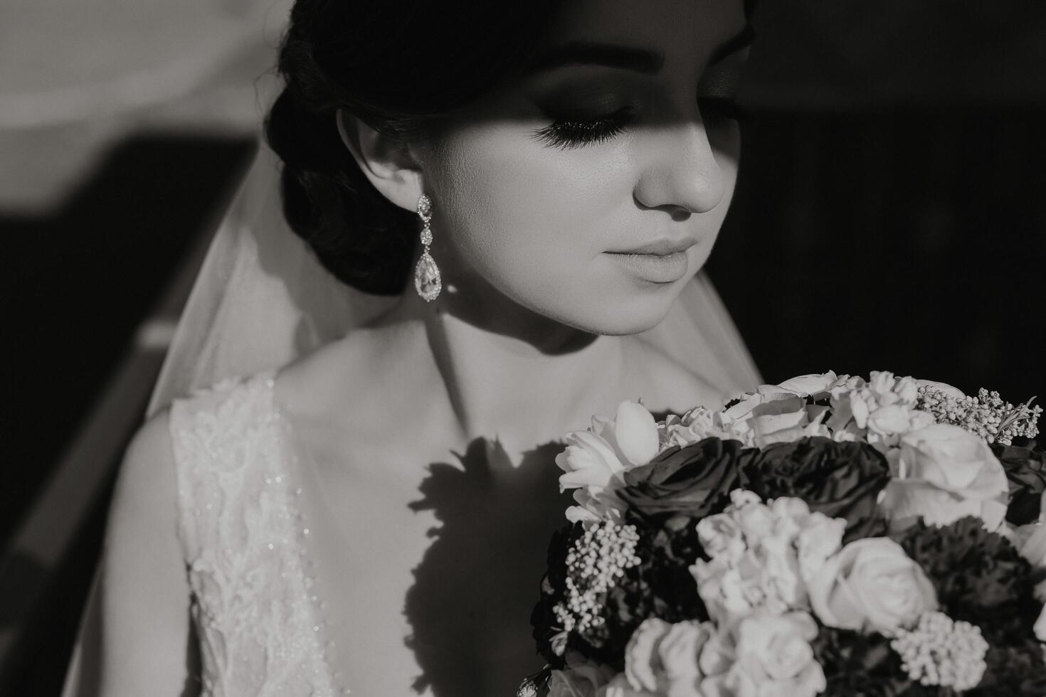 noir et blanc photo. le la mariée est en portant une bouquet, posant avec fermé yeux. préparation pour le fête. magnifique affronter. mariage cérémonie. lumière et ombre photo