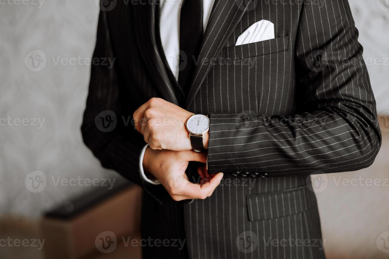 une fermer de une tondu Cadre de une homme met sur une regarder avec une cuir ceinture, est habillé dans une élégant costume, une blanc chemise, porte une or anneau. photo