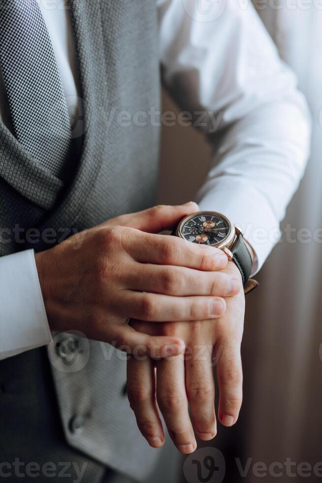 une fermer de une tondu Cadre de une homme met sur une regarder avec une cuir ceinture, est habillé dans une élégant costume, une blanc chemise, porte une or anneau. photo