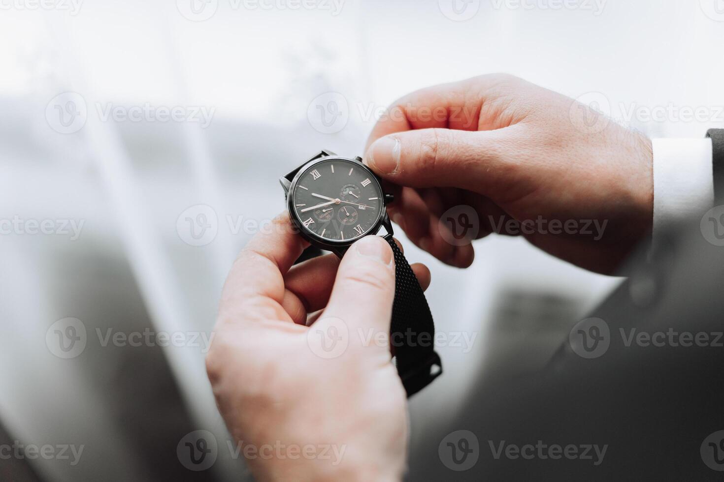 une fermer de une tondu Cadre de une homme met sur une regarder avec une cuir ceinture, est habillé dans une élégant costume, une blanc chemise, porte une or anneau. photo