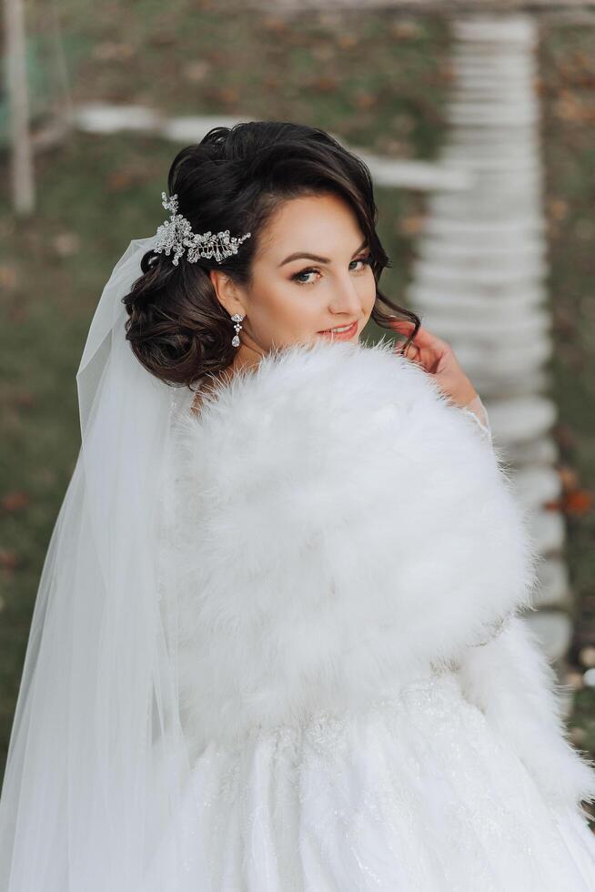 portrait. une brunette la mariée dans une robe et une voile, avec une élégant couronne, pose avec une bouquet. argent bijoux. magnifique maquillage et cheveux. l'automne mariage. fête photo