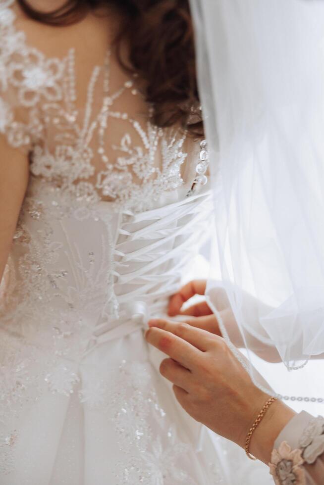 le Jeune la mariée est permanent de le dos. une magnifique femme dans une mariage robe, dans une pièce près une la fenêtre. attrayant fille dans une blanc mariage robe avec une longue train photo