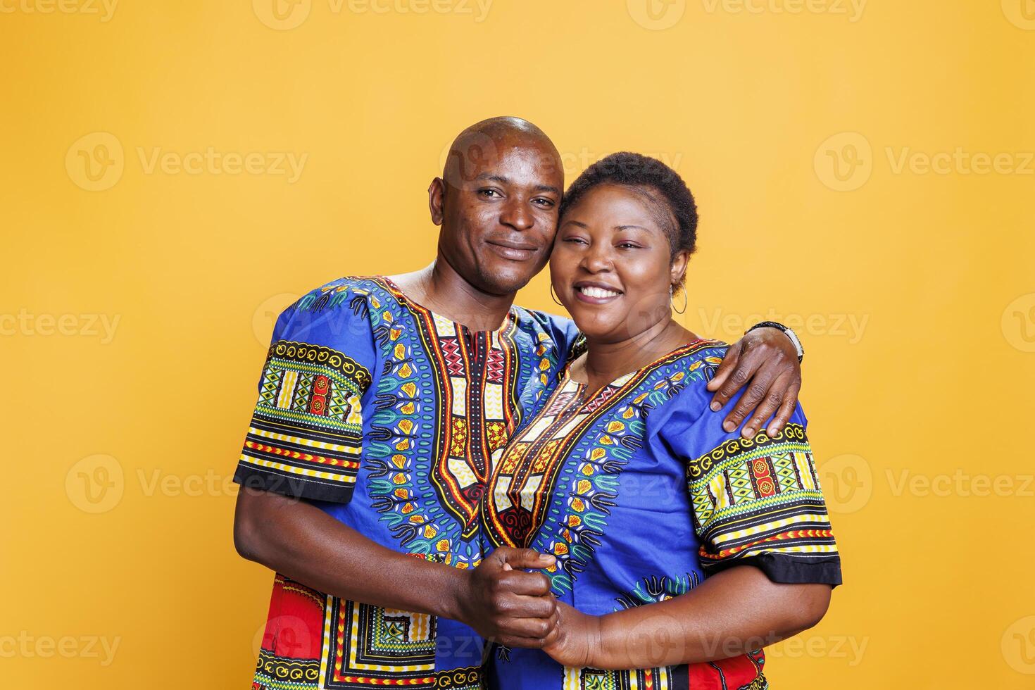 content africain américain romantique couple étreindre et à la recherche à caméra avec joyeux expression. souriant homme et femme portant ethnique vêtements étreindre et posant pour portrait sur Orange Contexte photo