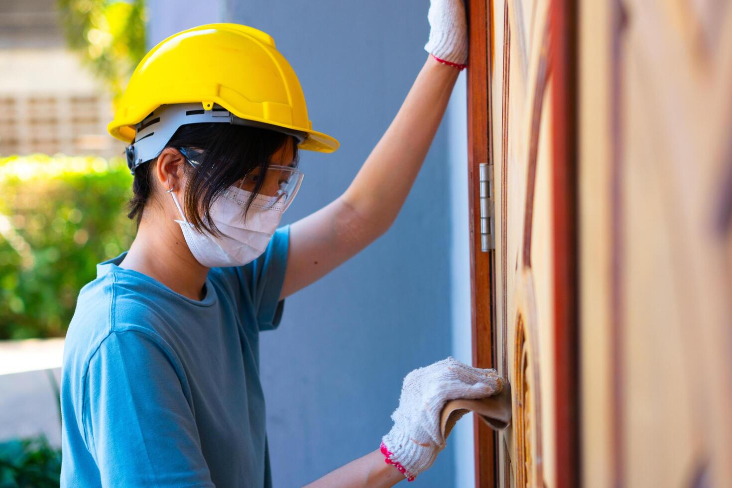 asiatique femelle ouvrier portant une sécurité casque en utilisant papier de verre à polonais une en bois porte à maison. photo