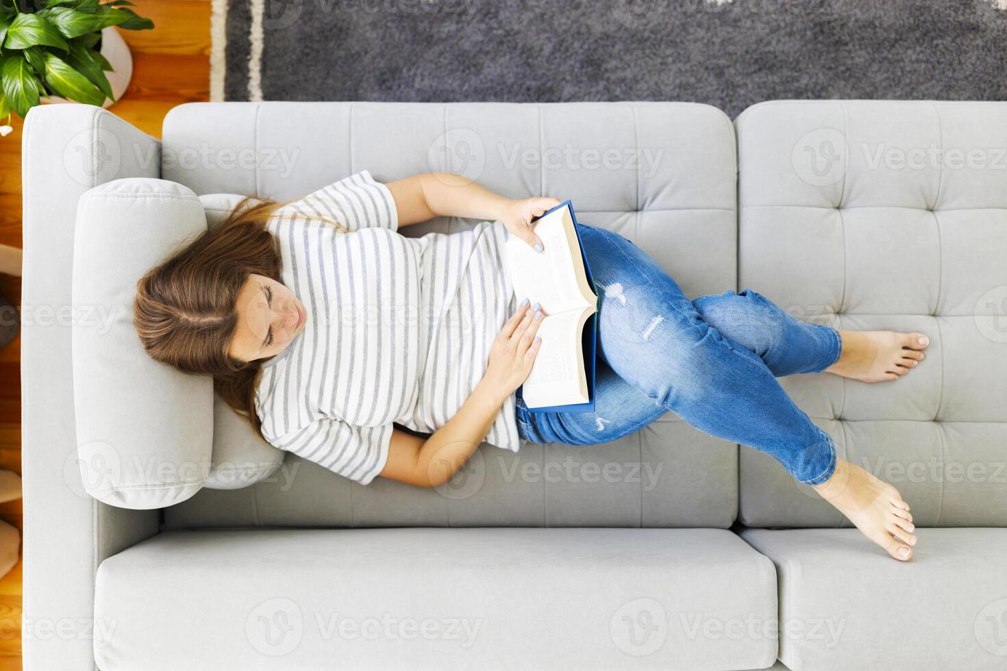 Haut vue de Jeune brunette femme relaxant sur canapé et en train de lire roman livre à Accueil photo