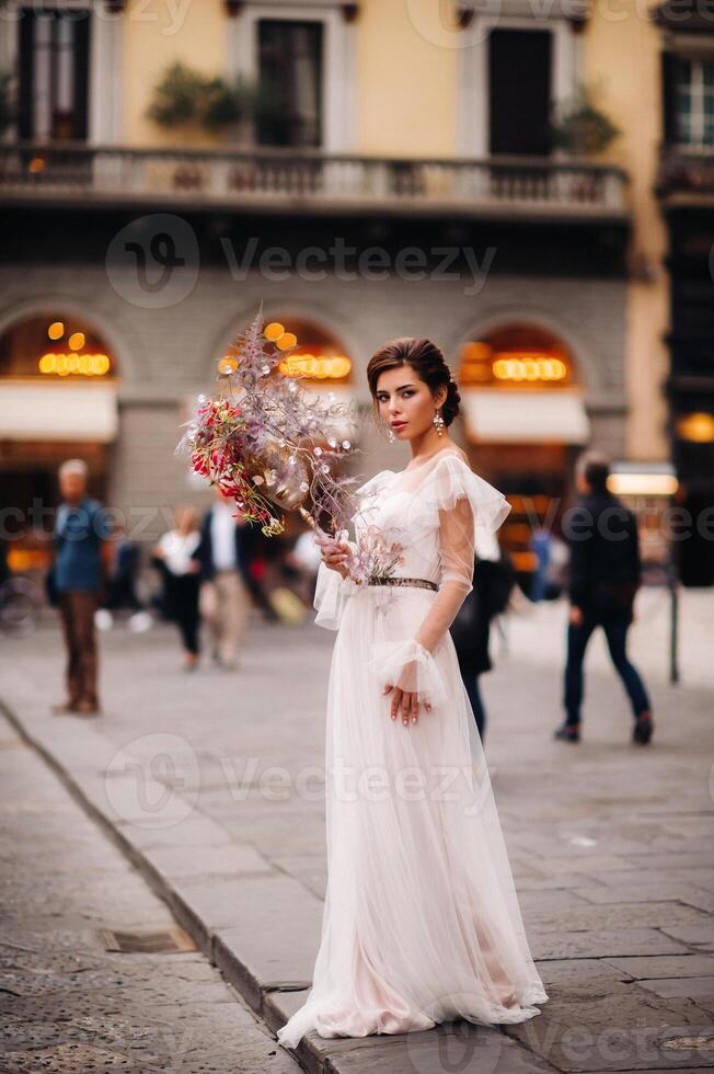 le fille-mariée est avec magnifique fleur modèle comme une masque dans Florence, élégant la mariée dans une mariage robe permanent avec une masque dans le vieux ville de Florence. modèle fille dans Florence photo