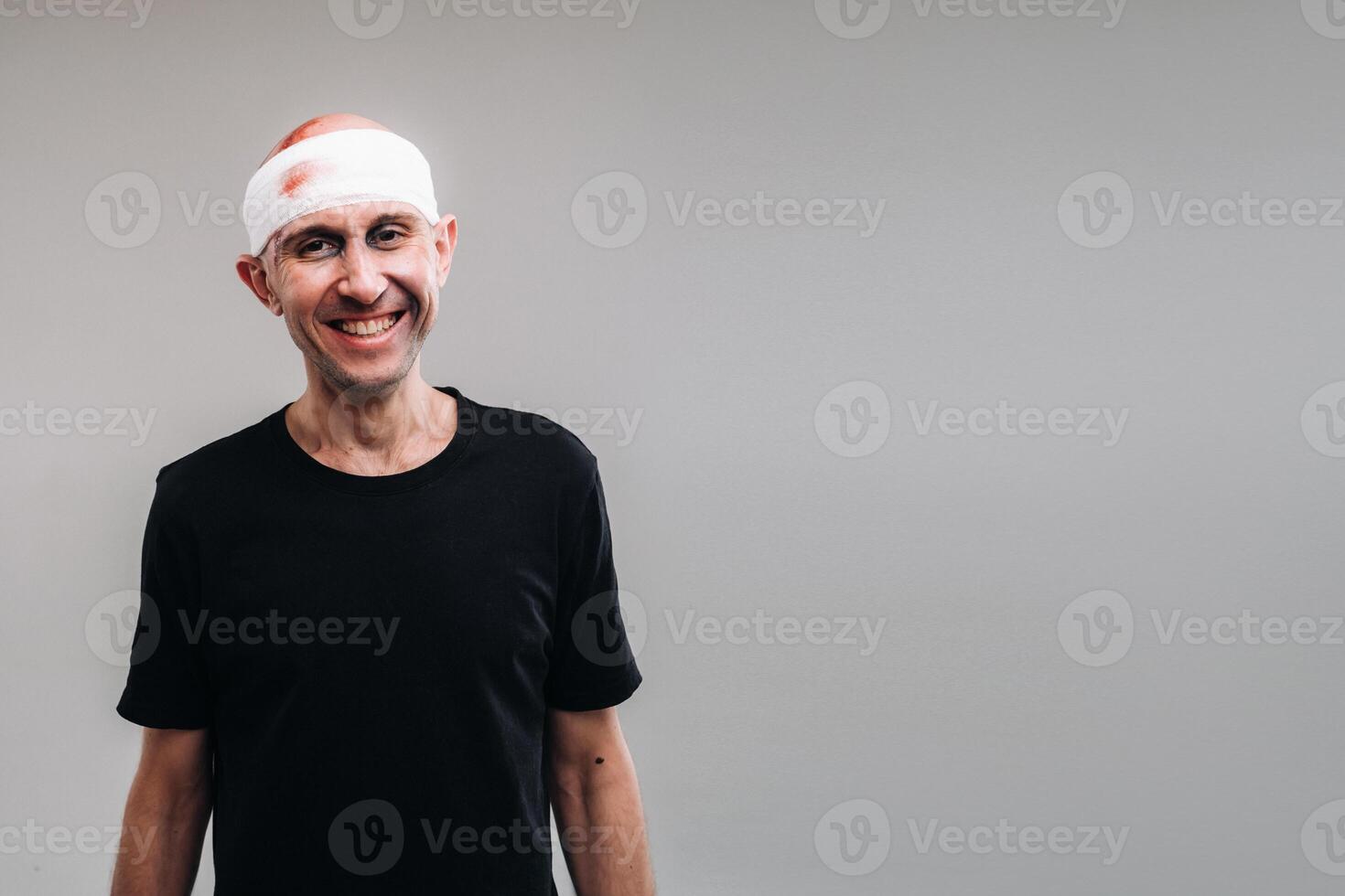 contre une gris Contexte des stands une battu et battu homme dans une noir T-shirt avec le sien tête enveloppé dans une bandage photo