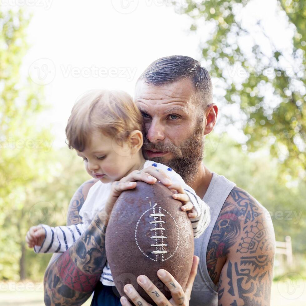 portrait de tatoué père et le sien fils dans le parc avec le rugby Balle photo