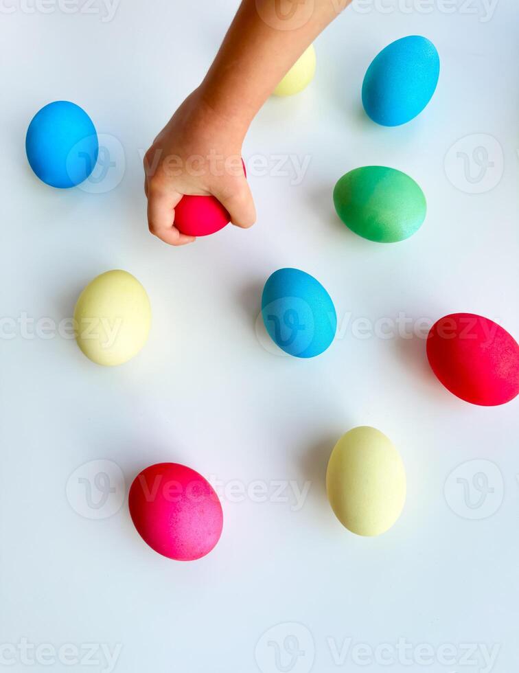 enfant main cueillette en haut bleu Pâques Oeuf parmi coloré des œufs sur blanc surface, interactif et engageant vacances activité concept. pouvez être utilisé pour éducatif contenu mise en évidence bien moteur photo