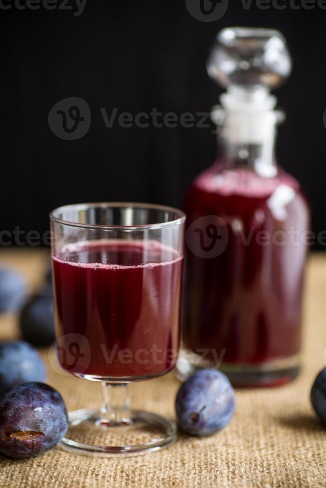 prune rouge du vin dans une verre et une carafe contre le Contexte de mûr grand prunes photo