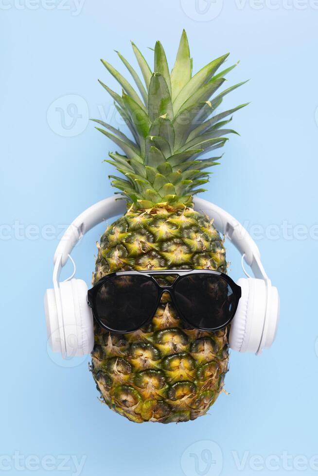 mûr ananas avec des lunettes de soleil et écouteurs sur bleu Contexte photo