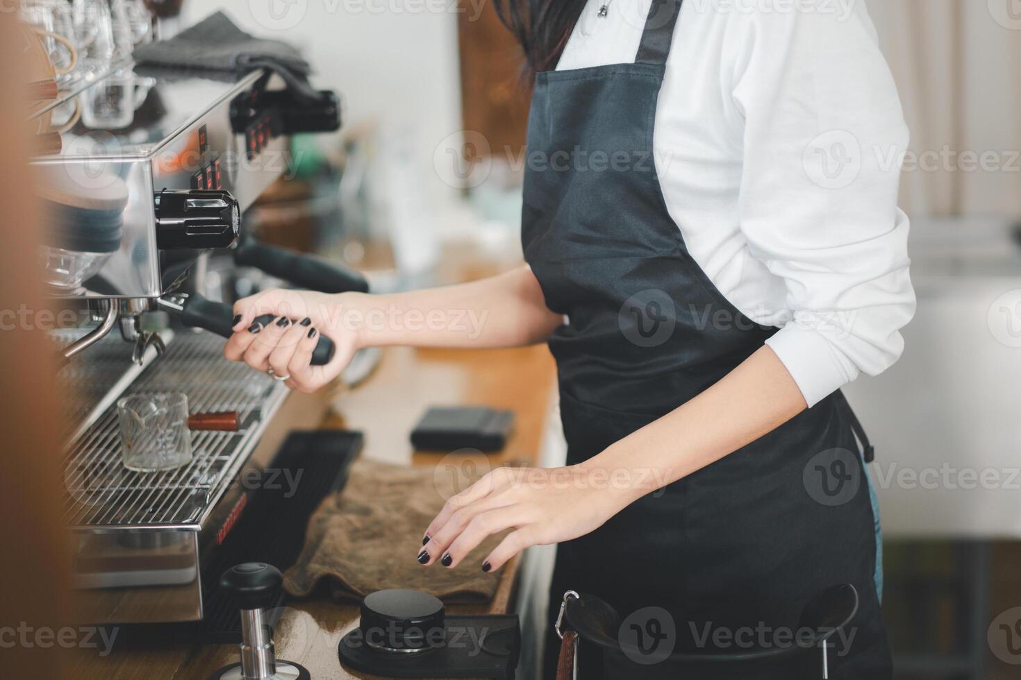 une qualifié barista dans une noir tablier habilement opère un Expresso machine, se concentrer sur artisanat le parfait tasse de café. photo