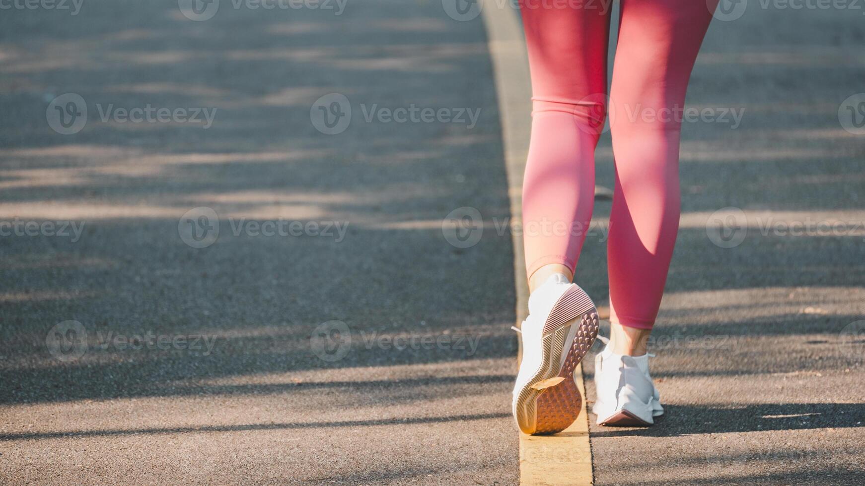 fermer de une coureur jambes dans vibrant rose leggings, soulignant mouvement et aptitude sur une ensoleillé asphalte route. photo