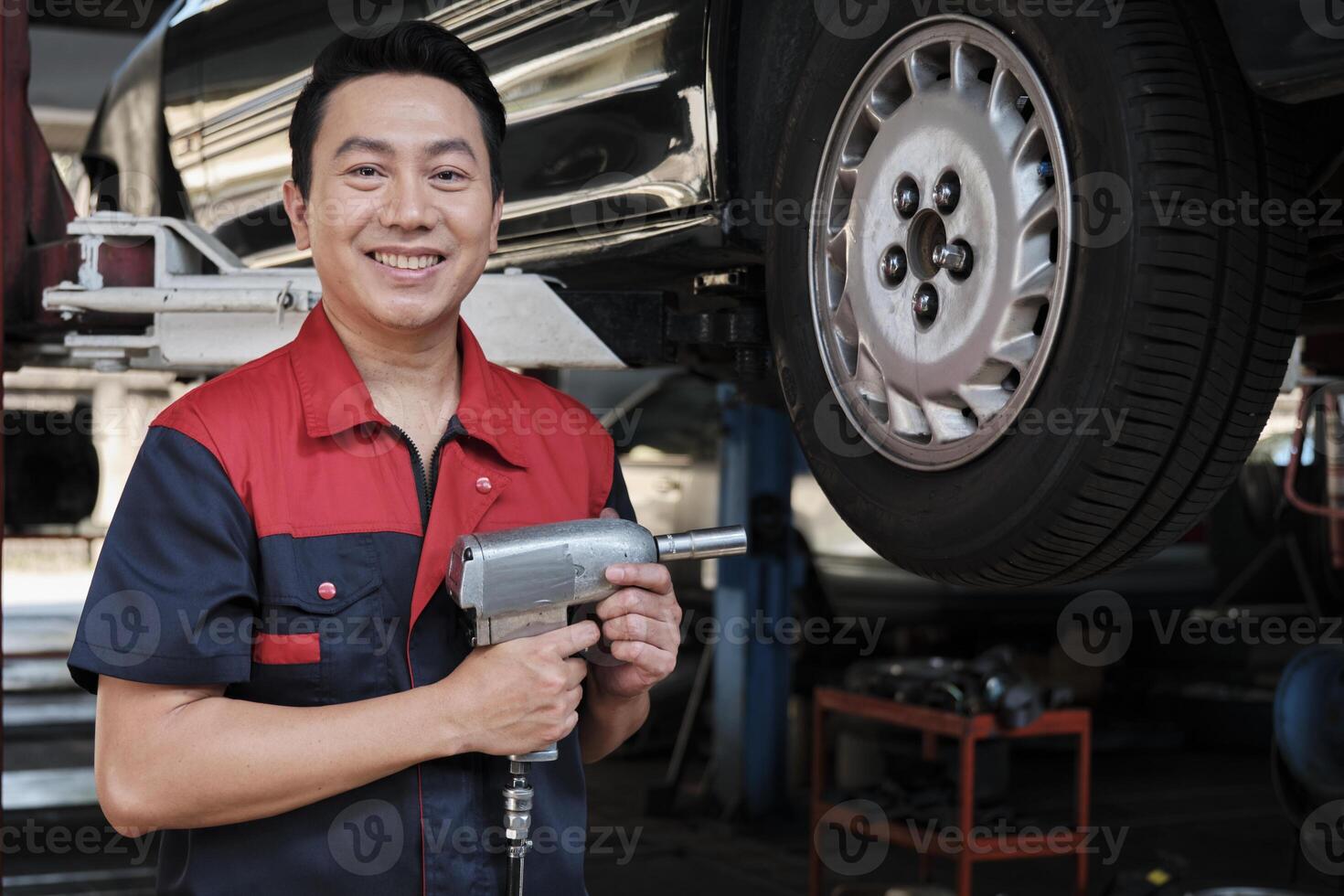 un expert asiatique Masculin automobile mécanicien technicien est baise voiture roue des noisettes sur levage avec percer clé pour réparation à garage. véhicule entretien un service travaux industrie Occupation affaires emplois. photo