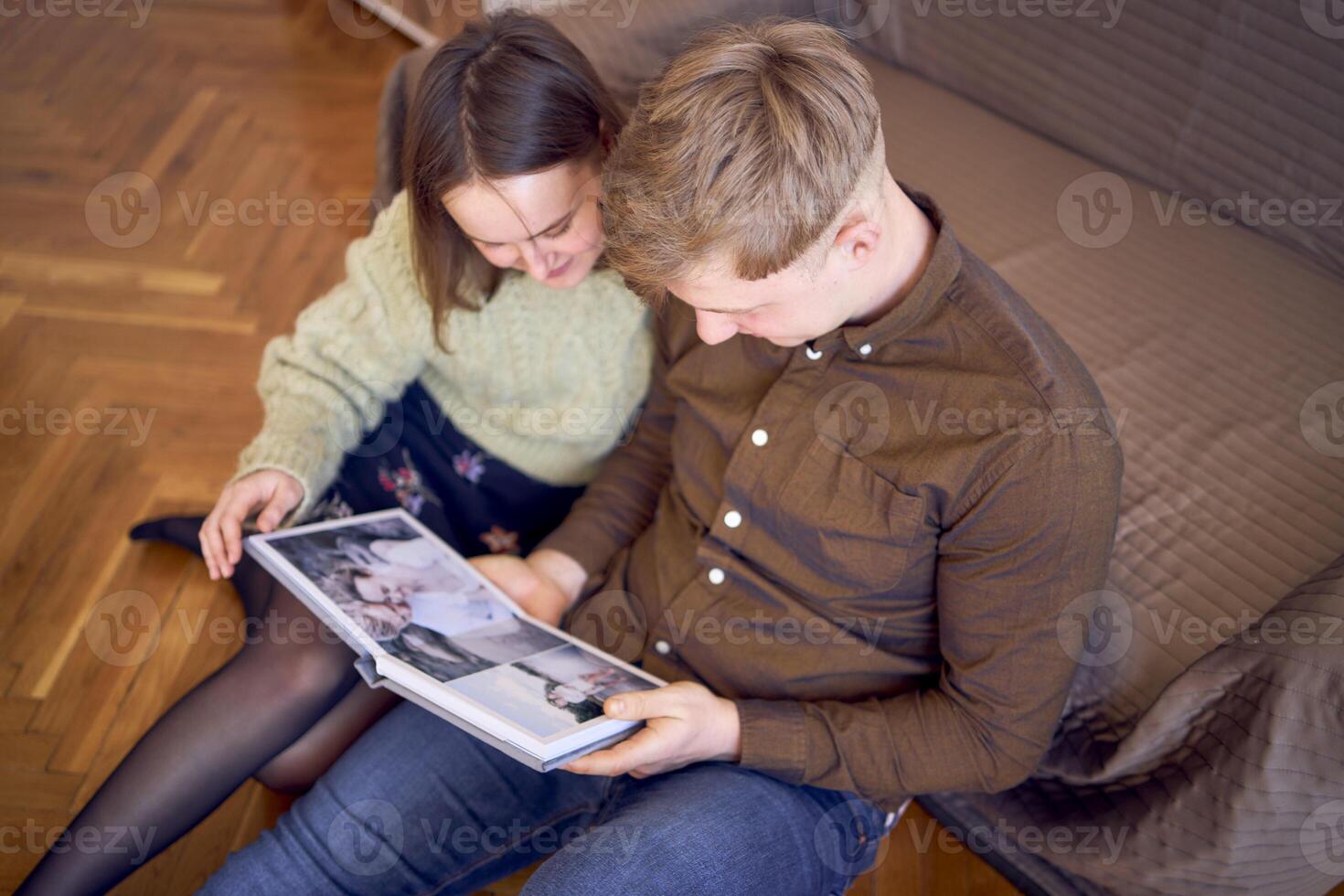 Jeune couple à la recherche à leur mariage photo album par le lit dans vivant chambre, cockapoo fonctionnement autour