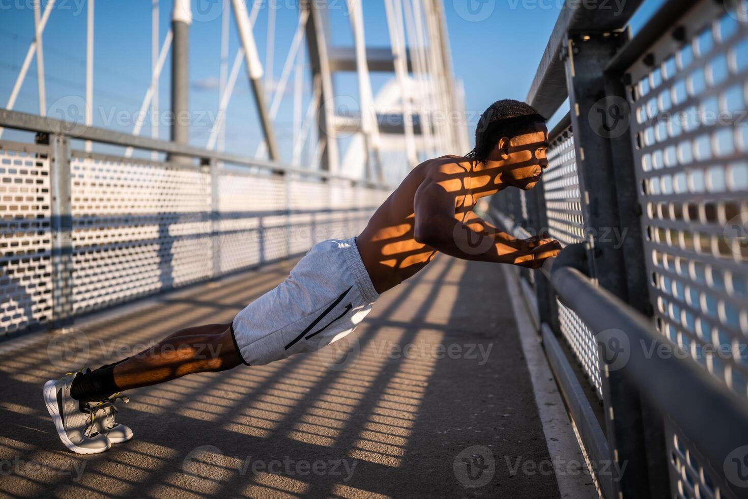 Jeune Afro-américain homme est exercice sur le pont dans le ville. il est Faire des pompes. photo