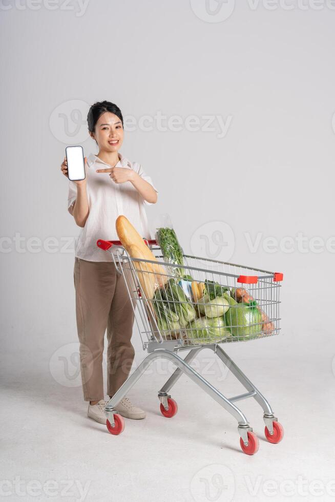 souriant femme Heureusement pousser une supermarché Chariot, isolé sur blanc Contexte photo