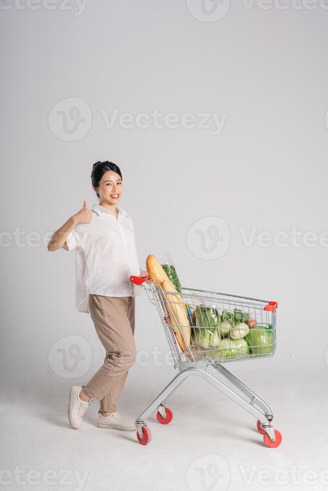 souriant femme Heureusement pousser une supermarché Chariot, isolé sur blanc Contexte photo