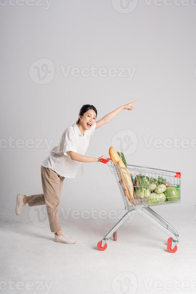 souriant femme Heureusement pousser une supermarché Chariot, isolé sur blanc Contexte photo
