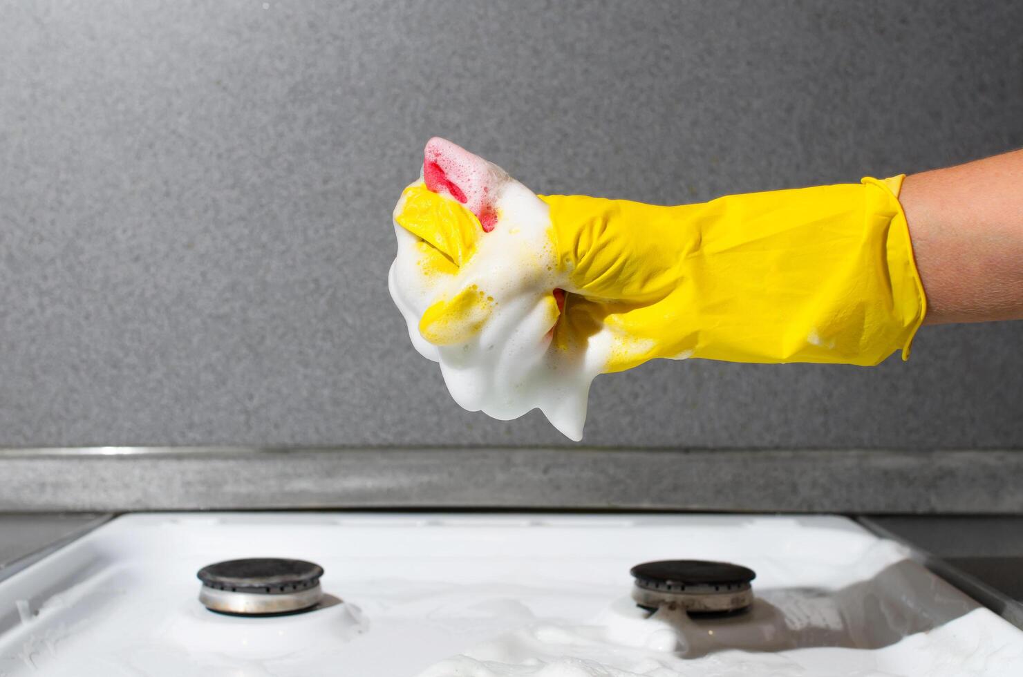femme main dans gant nettoyage gaz poêle. femme serre mousse de éponge. cuisine nettoyage, Ménage corvées photo