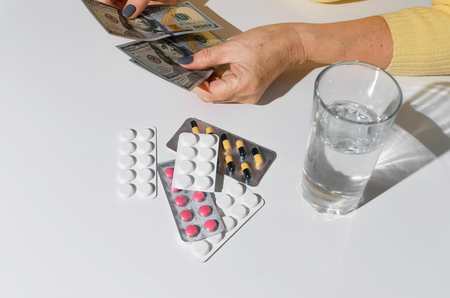 personnes âgées femme mains en portant argent. comprimés et verre de l'eau sur blanc table Haut voir. concept de traitement coût, médicament prix, santé Assurance budget photo