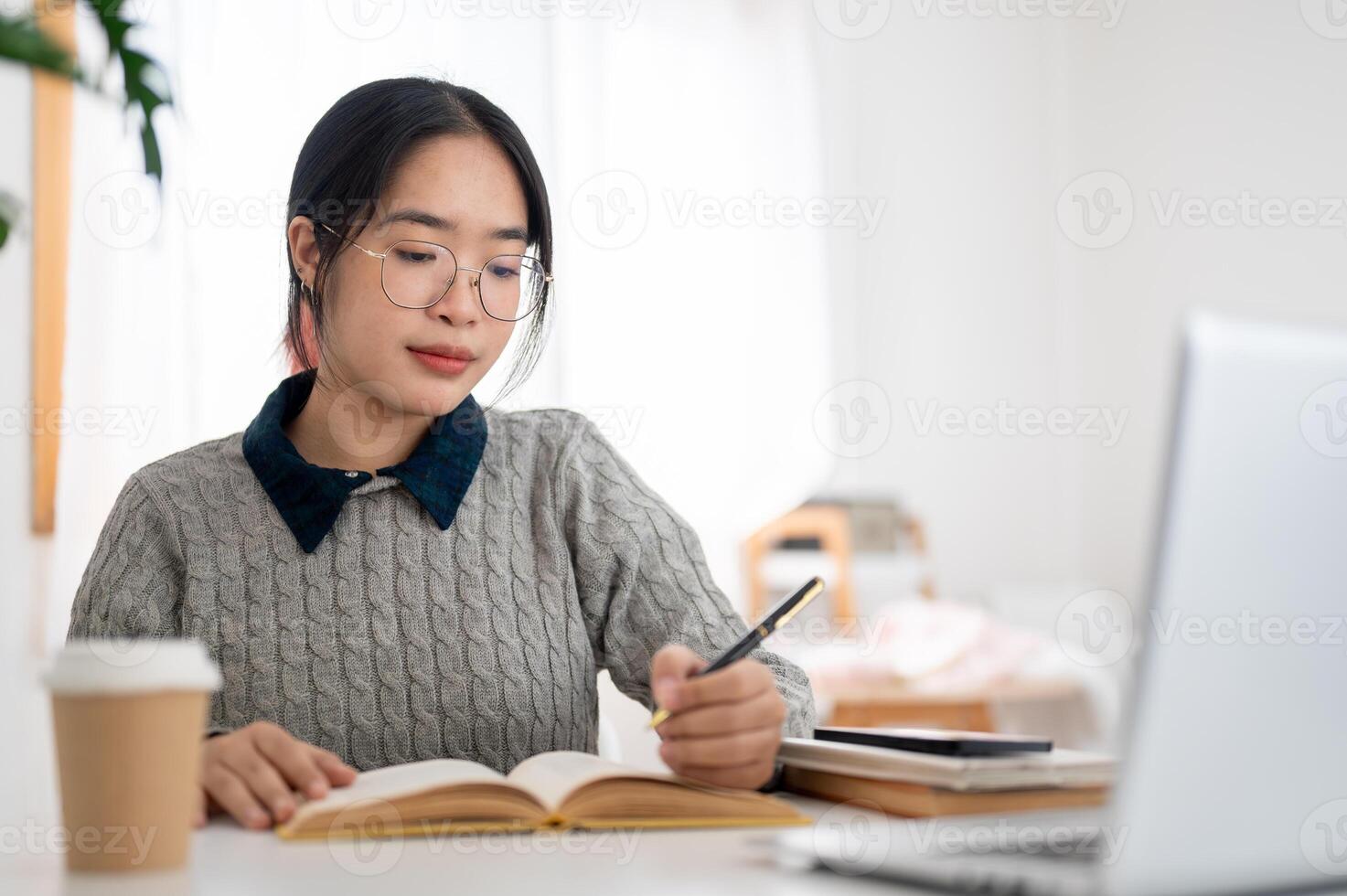 une Jeune asiatique femelle étudiant est se concentrer sur sa devoirs et en train de lire livre à une table dans sa chambre. photo